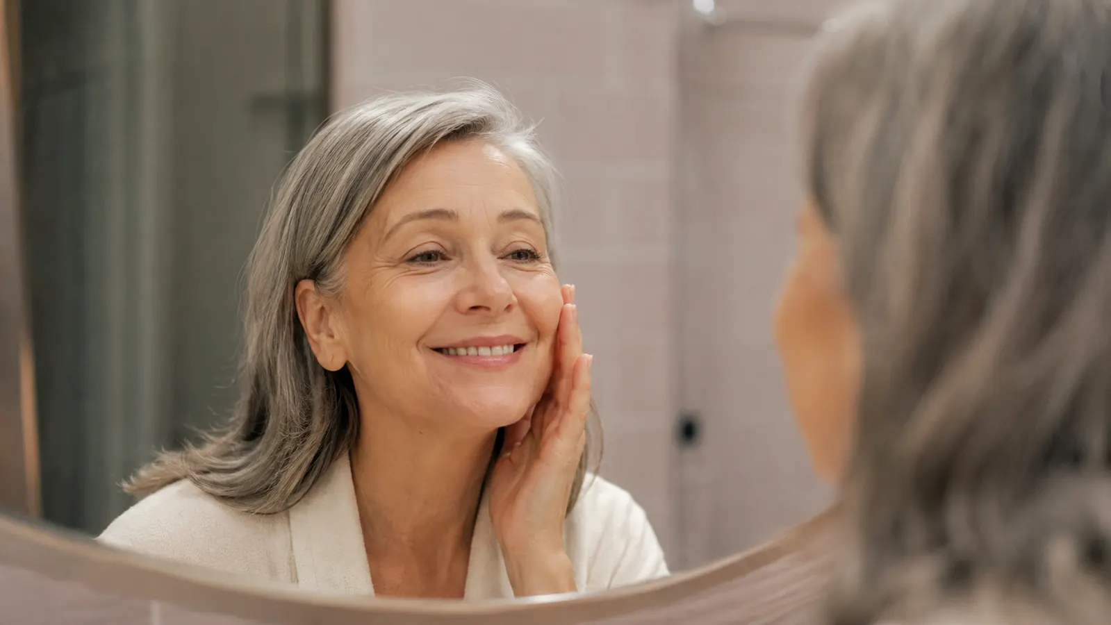 Woman looking at her glowing skin in a bathroom mirror the morning after using a hydrogel mask