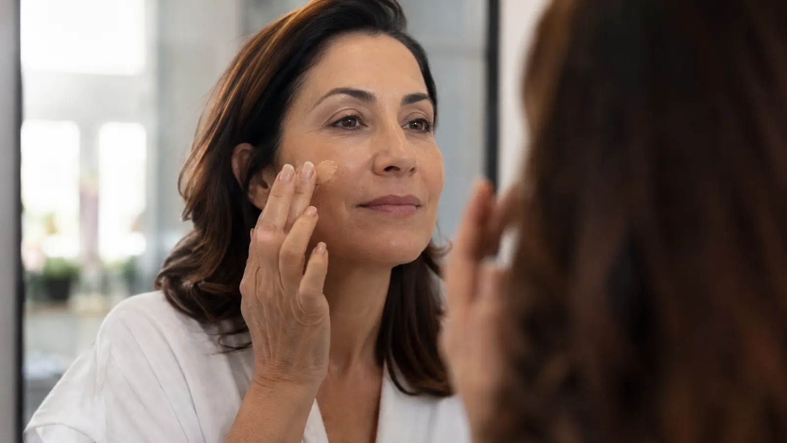 Woman applying foundation makeup smoothly to freshly dermaplaned skin in natural light