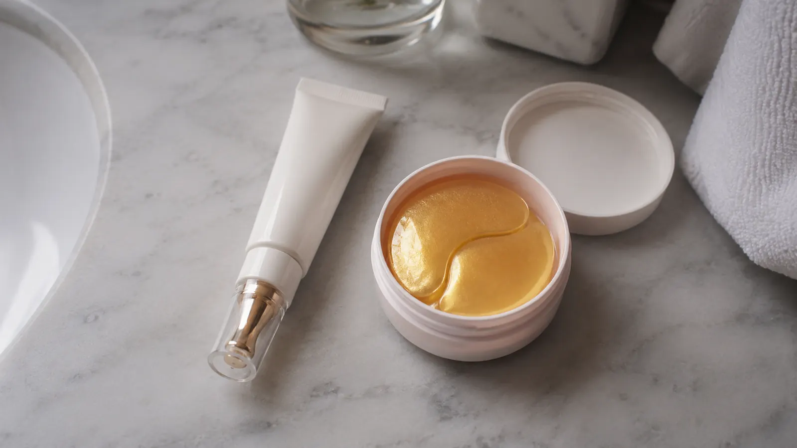 Bathroom counter flat lay with a jar of eye cream and a box of gold eye patches side by side