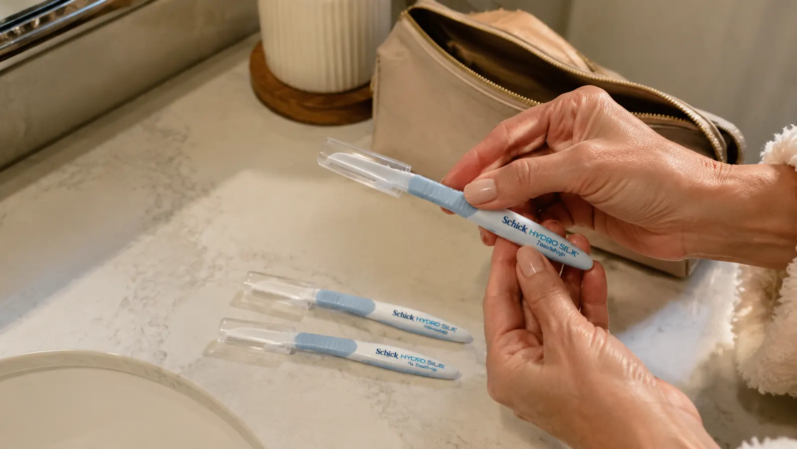Three dermaplaning razors with precision covers laid out on a bathroom counter next to a makeup bag